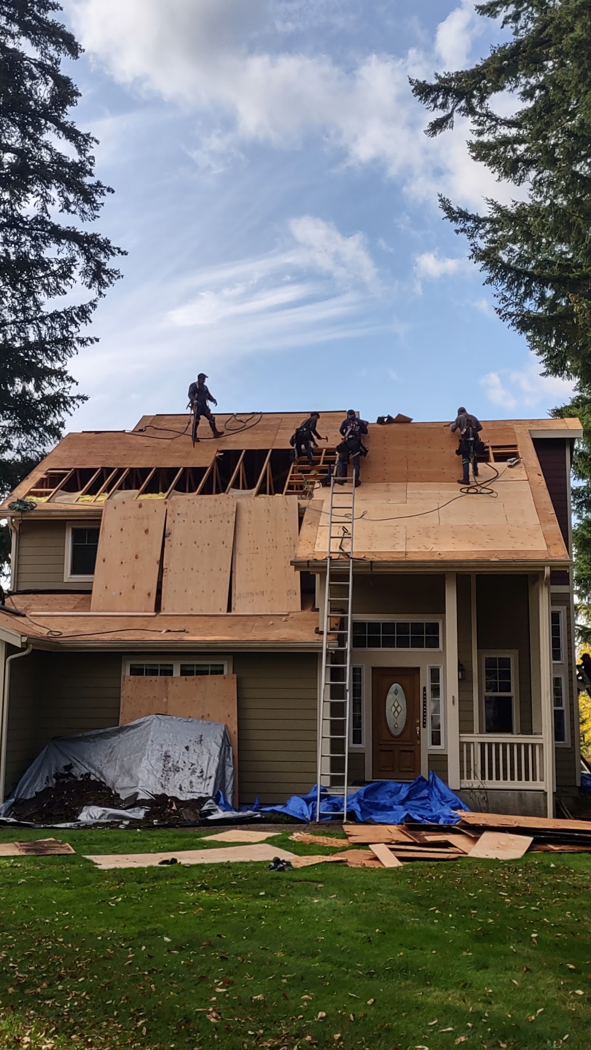 A four person roofing crew in safety harnesses tearing off and re-decking a large roof