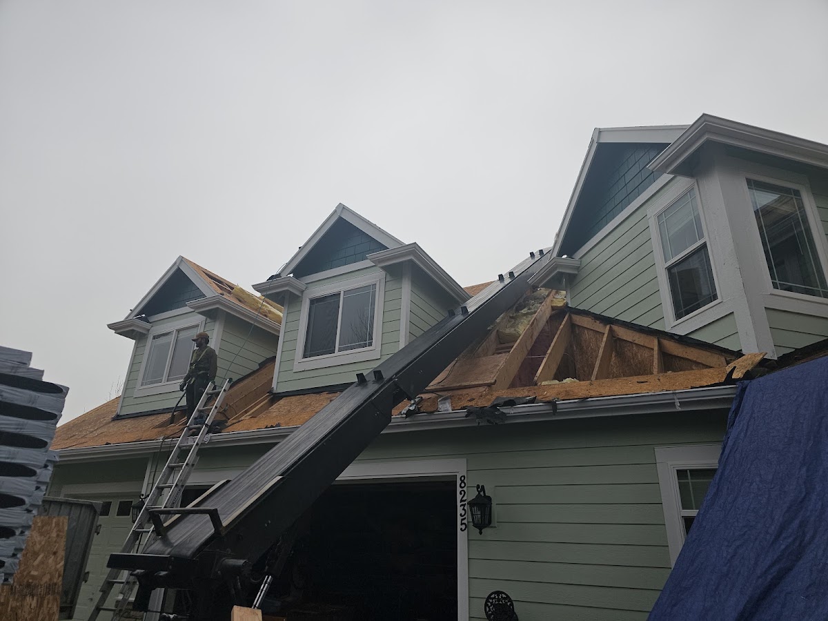 A roofer working on plywood roof sheathing with dormers exposed during a tear-off