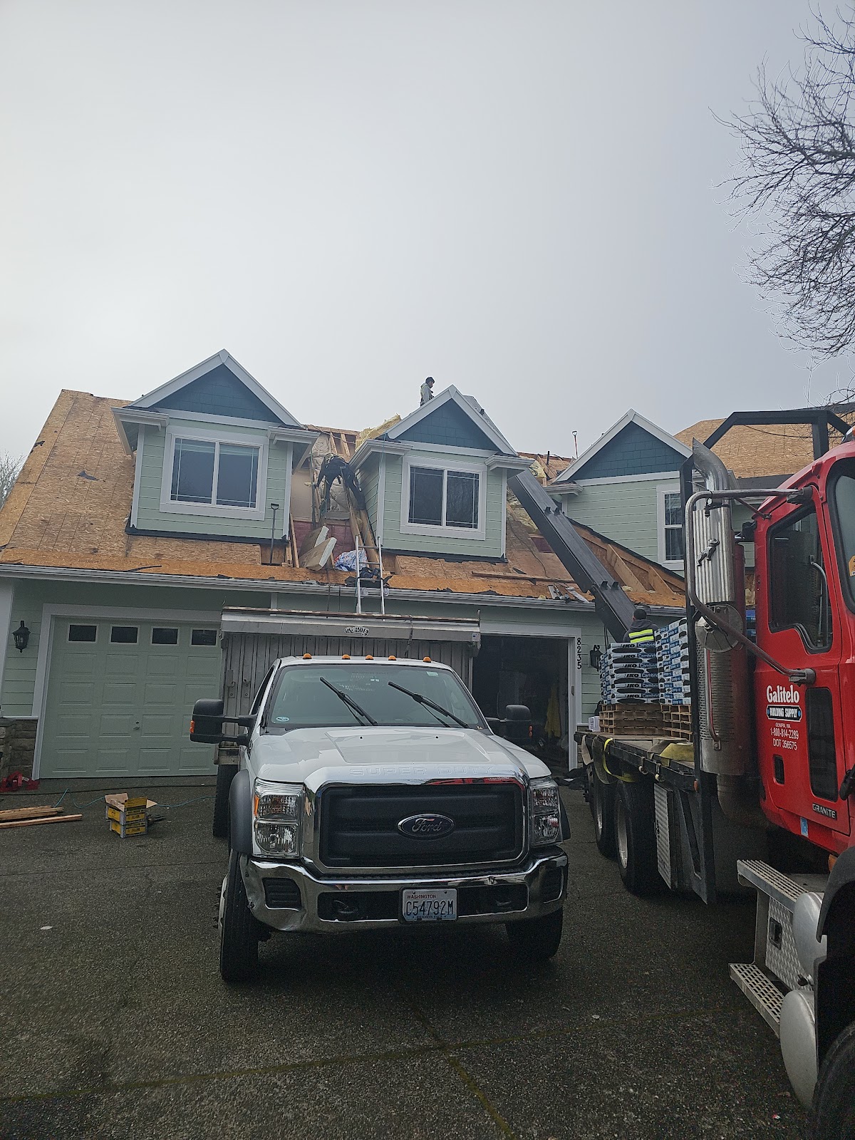 A delivery truck unloading roofing material at a job site