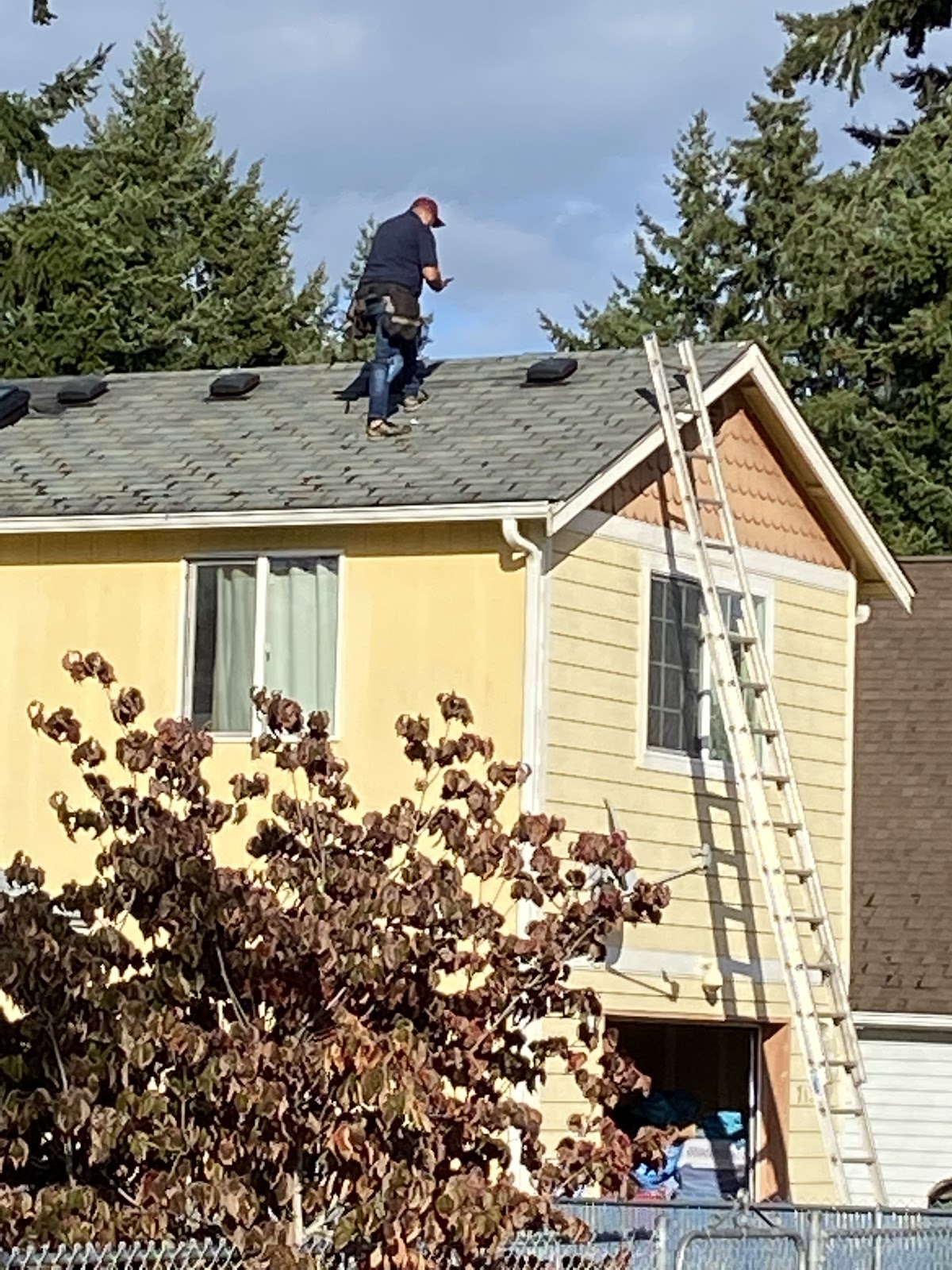A roofer working on the roof of a home with a ladder against the gable